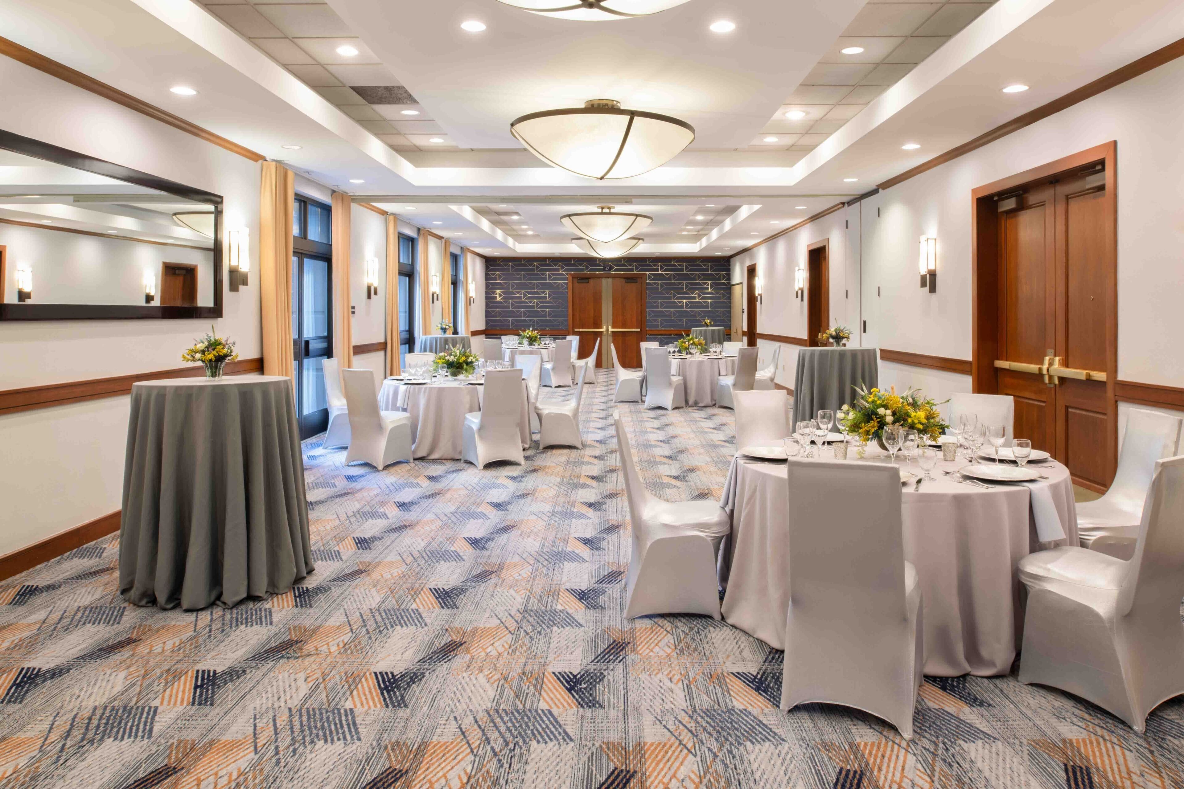 A hotel conference room with round tables, white chairs, and a patterned carpet.
