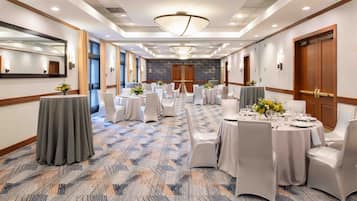 A hotel conference room with round tables, white chairs, and a patterned carpet.
