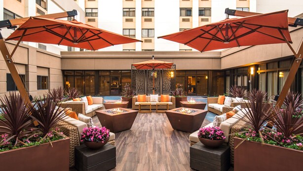 A modern outdoor lounge area with seating, fire pits, and large umbrellas.