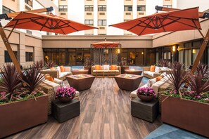 Un área lounge moderna al aire libre con asientos, fogones y sombrillas grandes.