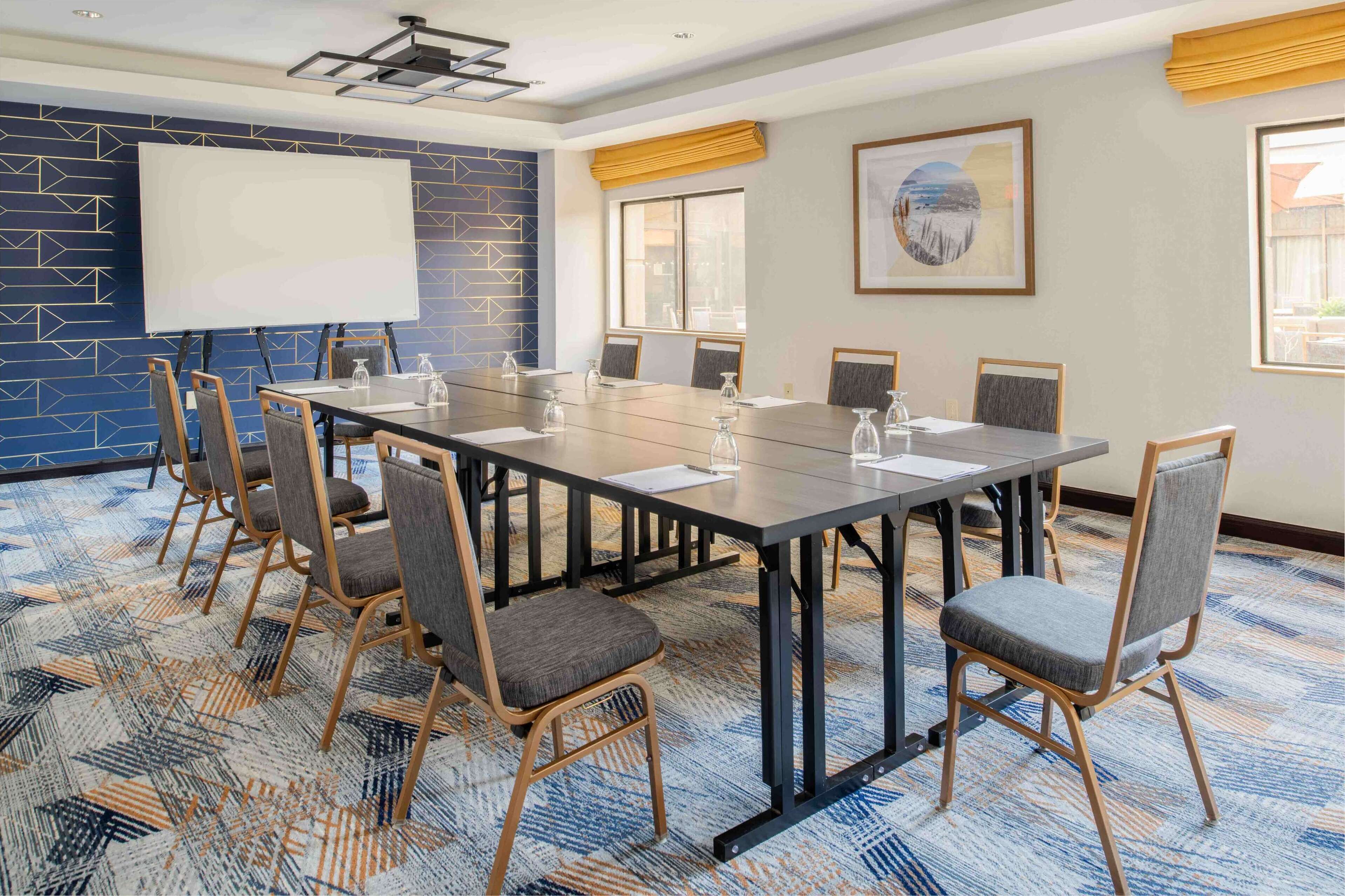 A conference room with a large table, chairs, a projector screen, and a carpeted floor.