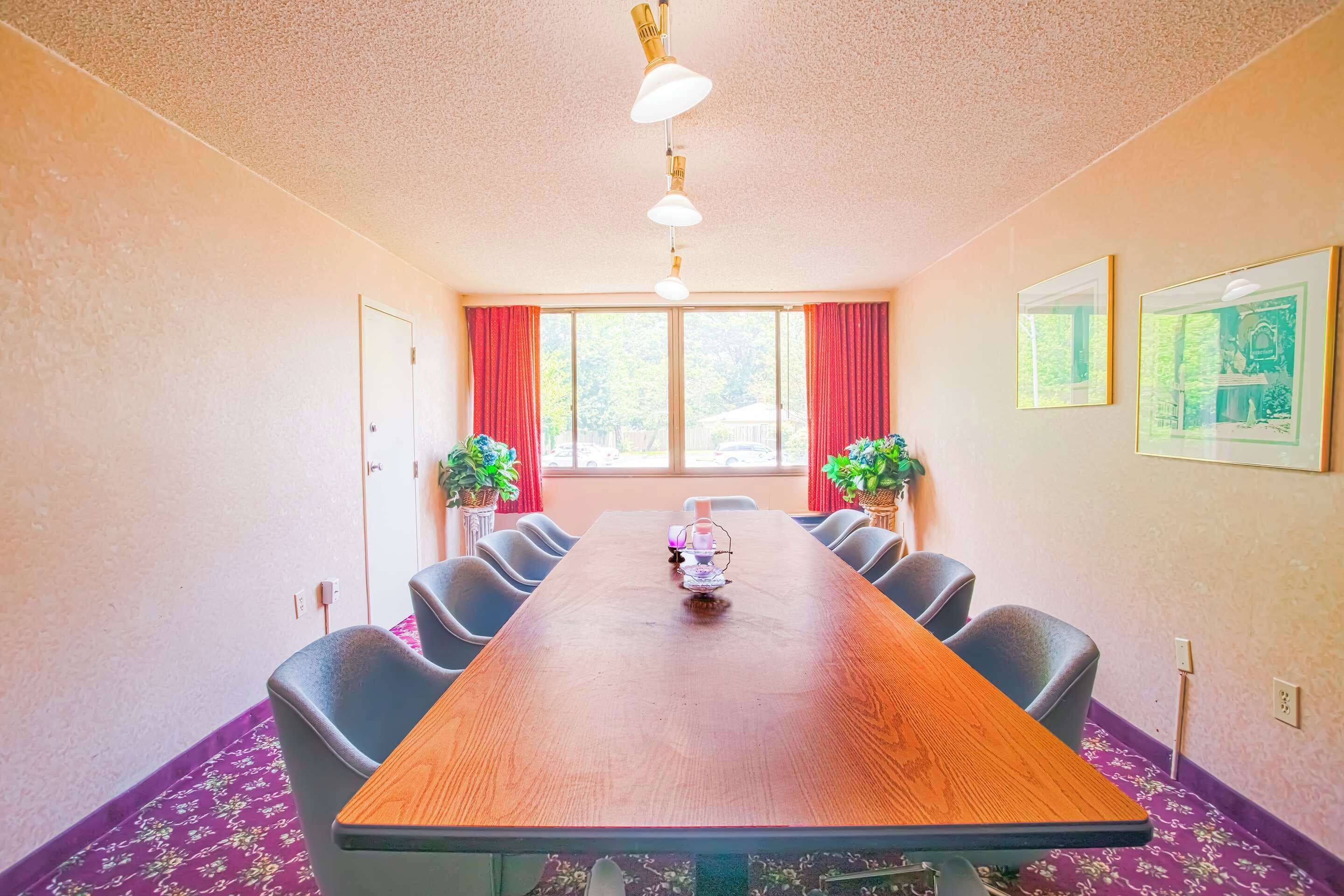 Een vergaderruimte met een lange houten tafel, zes stoelen, twee potplanten en ingelijste foto's aan de muren.
