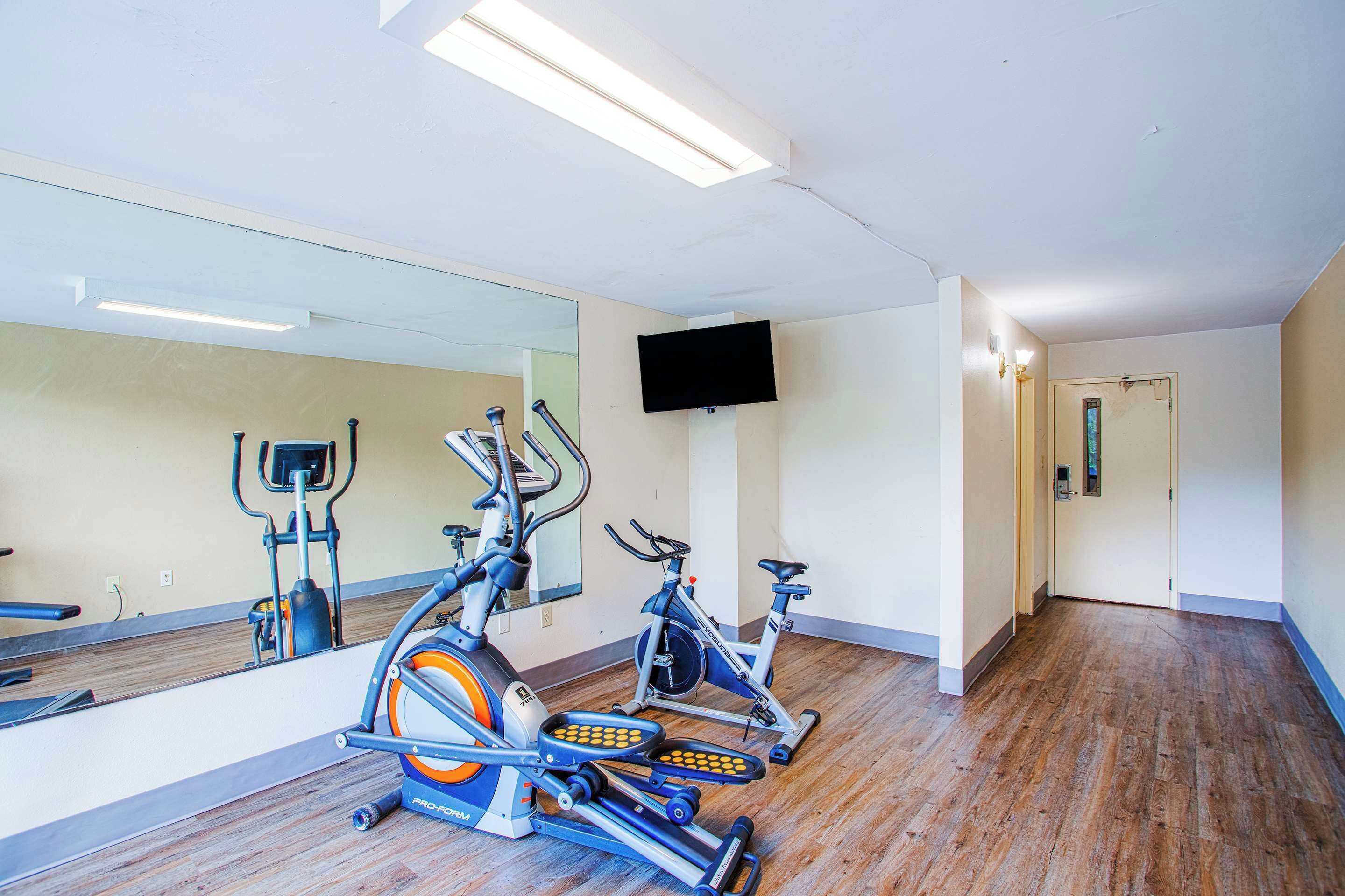 A gym with exercise bikes, a mirrored wall, and a TV on the wall.