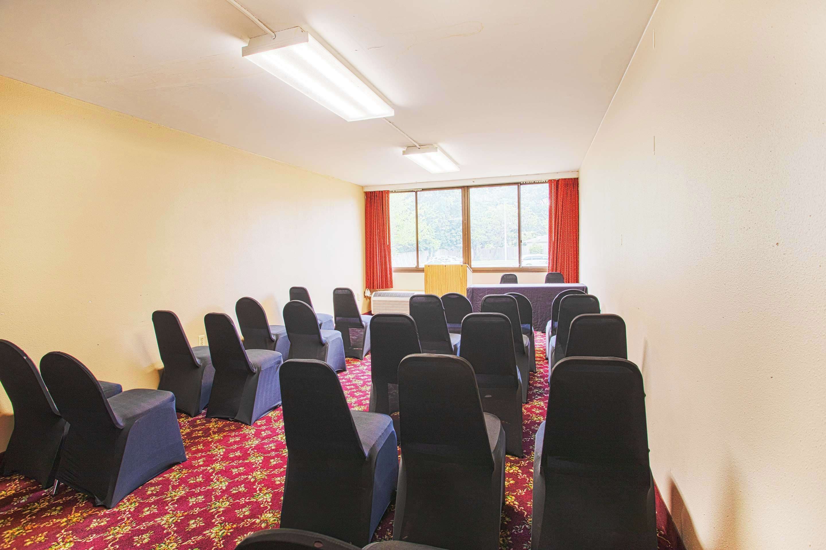A conference room with rows of chairs, a projector, and a large window with curtains.