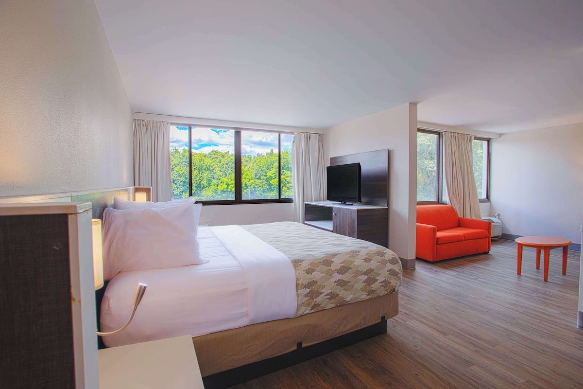 A hotel room with a bed, a TV, a red chair, and a small table.