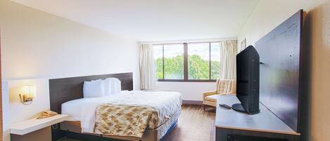 Habitación de hotel con cama, escritorio con ordenador, televisor y ventana con cortinas.