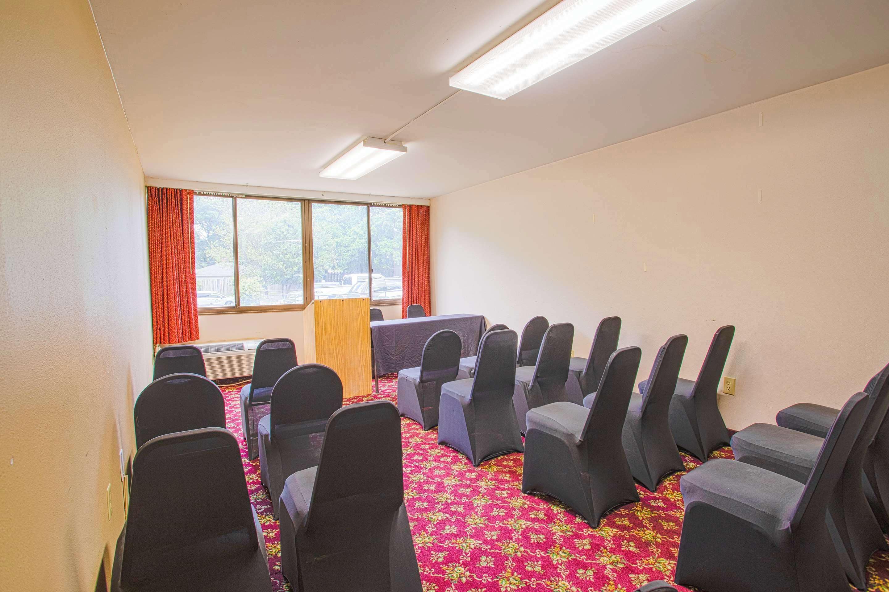 A conference room with rows of chairs, a podium, and a large window with curtains.