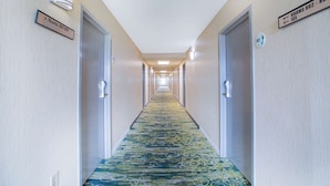 A hotel hallway with carpeted floors, doors on both sides, and directional signs for rooms and ice.