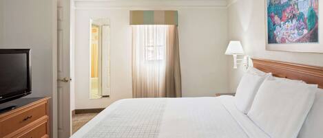 Habitación de hotel con una cama grande, un televisor sobre un aparador de madera, un cuadro en la pared y una ventana con cortinas.