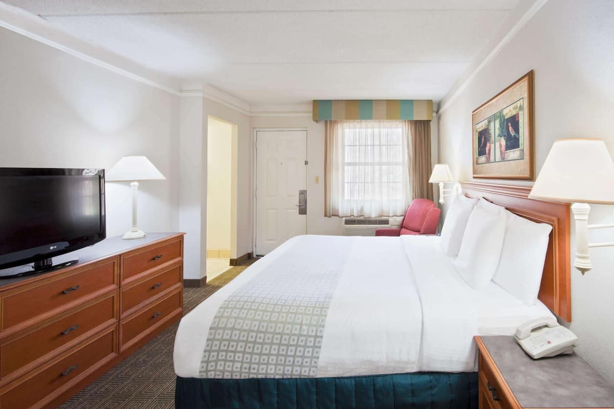 Une chambre d’hôtel avec un grand lit, un téléviseur posé sur une commode en bois, une table de chevet avec une lampe et un tableau accroché au mur.