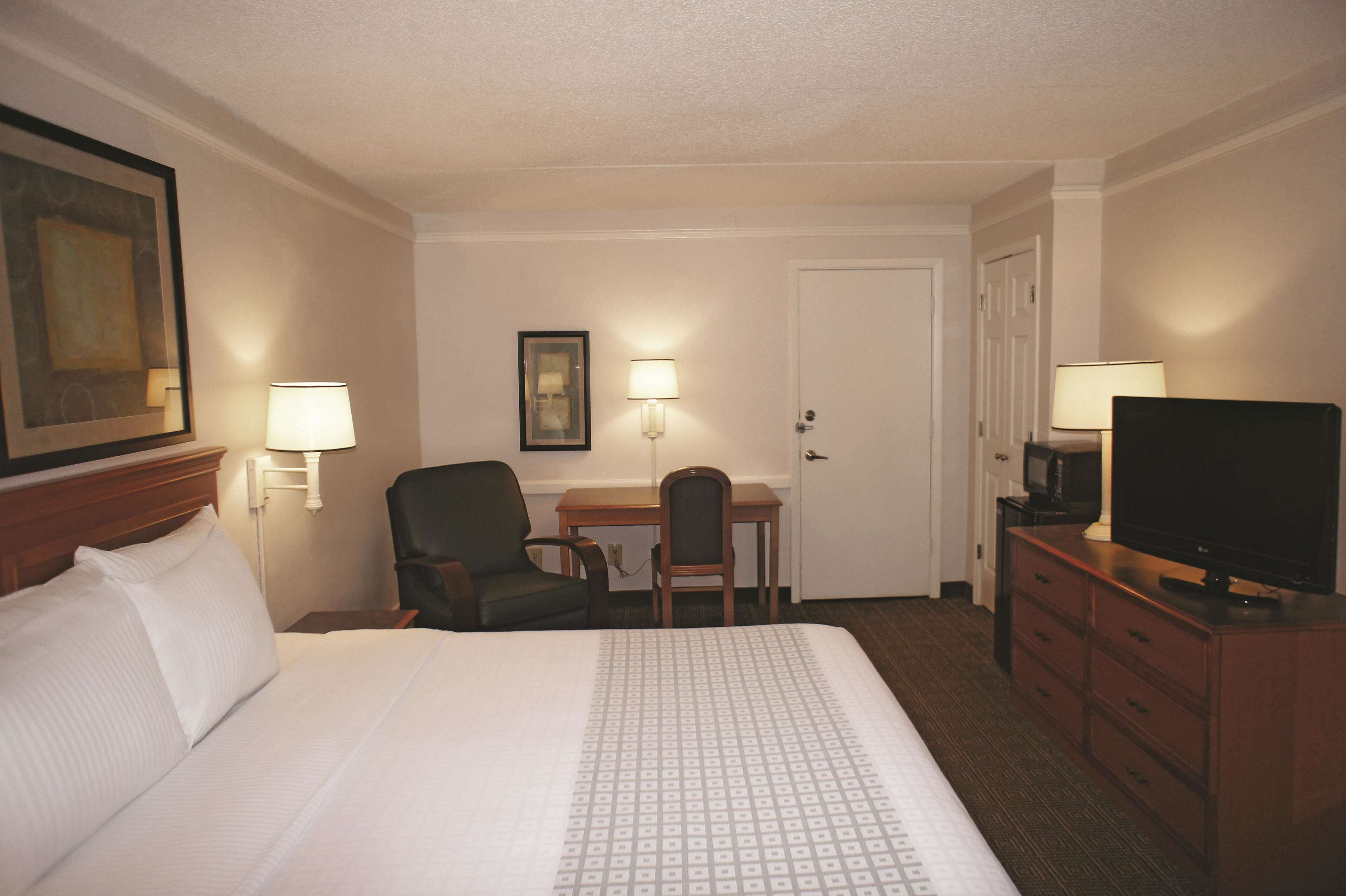 A hotel room with a large bed, a desk, a chair, a television, and two wall-mounted lamps.