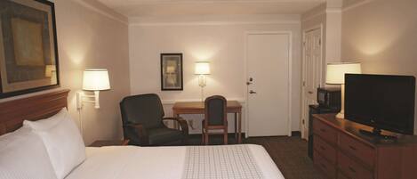 A hotel room with a large bed, a desk, a chair, a television, and two wall-mounted lamps.