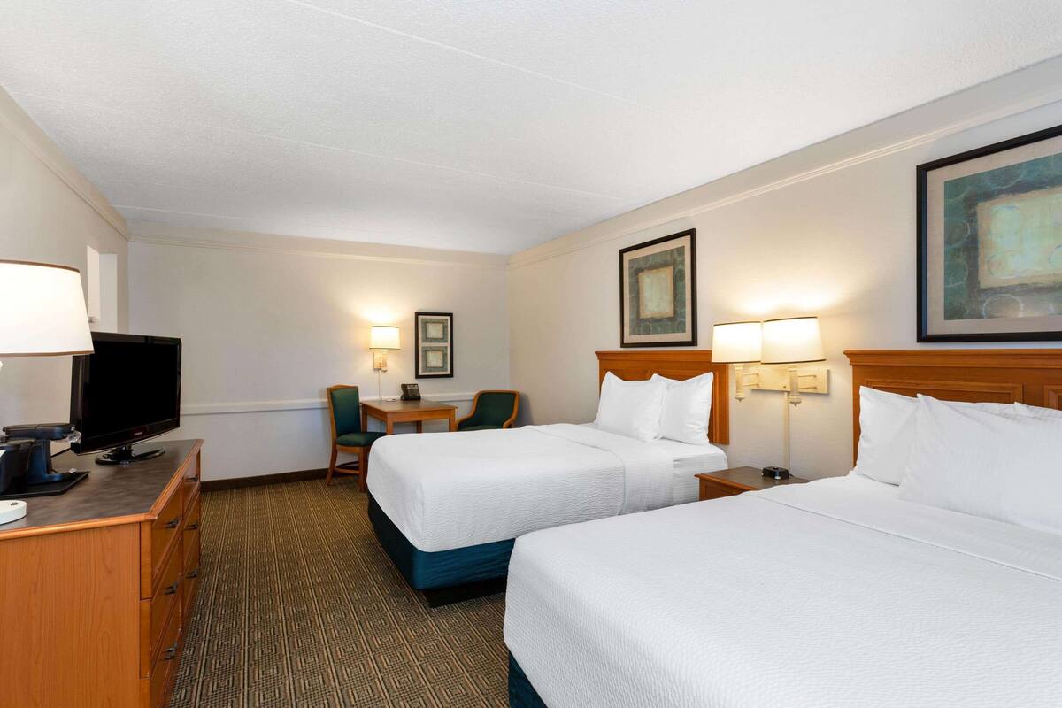 Ein Hotelzimmer mit zwei Betten, einem Schreibtisch mit Fernseher und einem kleinen Tisch mit Stuhl.