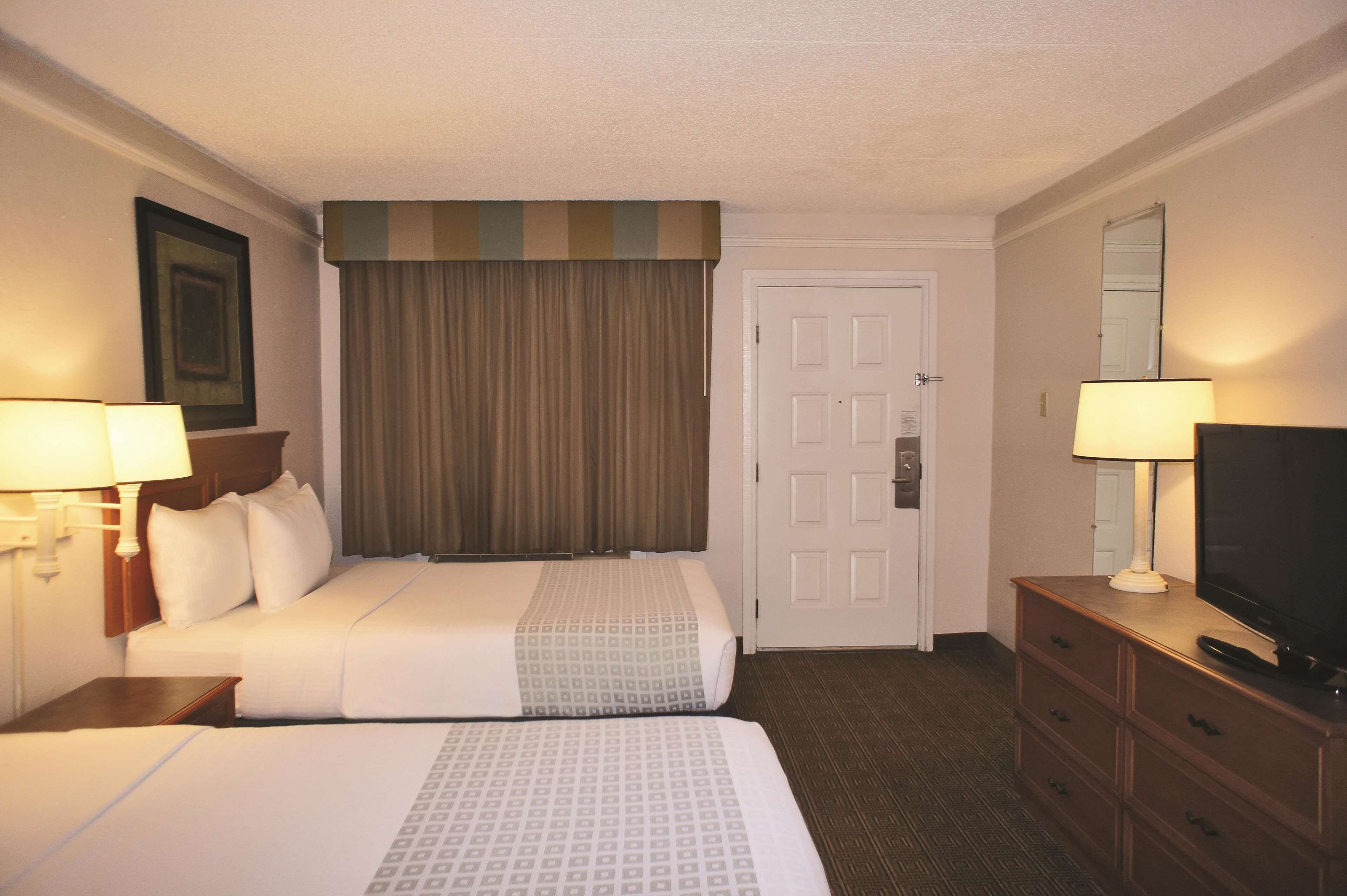 A hotel room with two beds, a television, a dresser, a door, and a window with curtains.