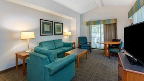 A hotel room with a teal sofa set, a wooden coffee table, a TV, and a dining table with chairs.