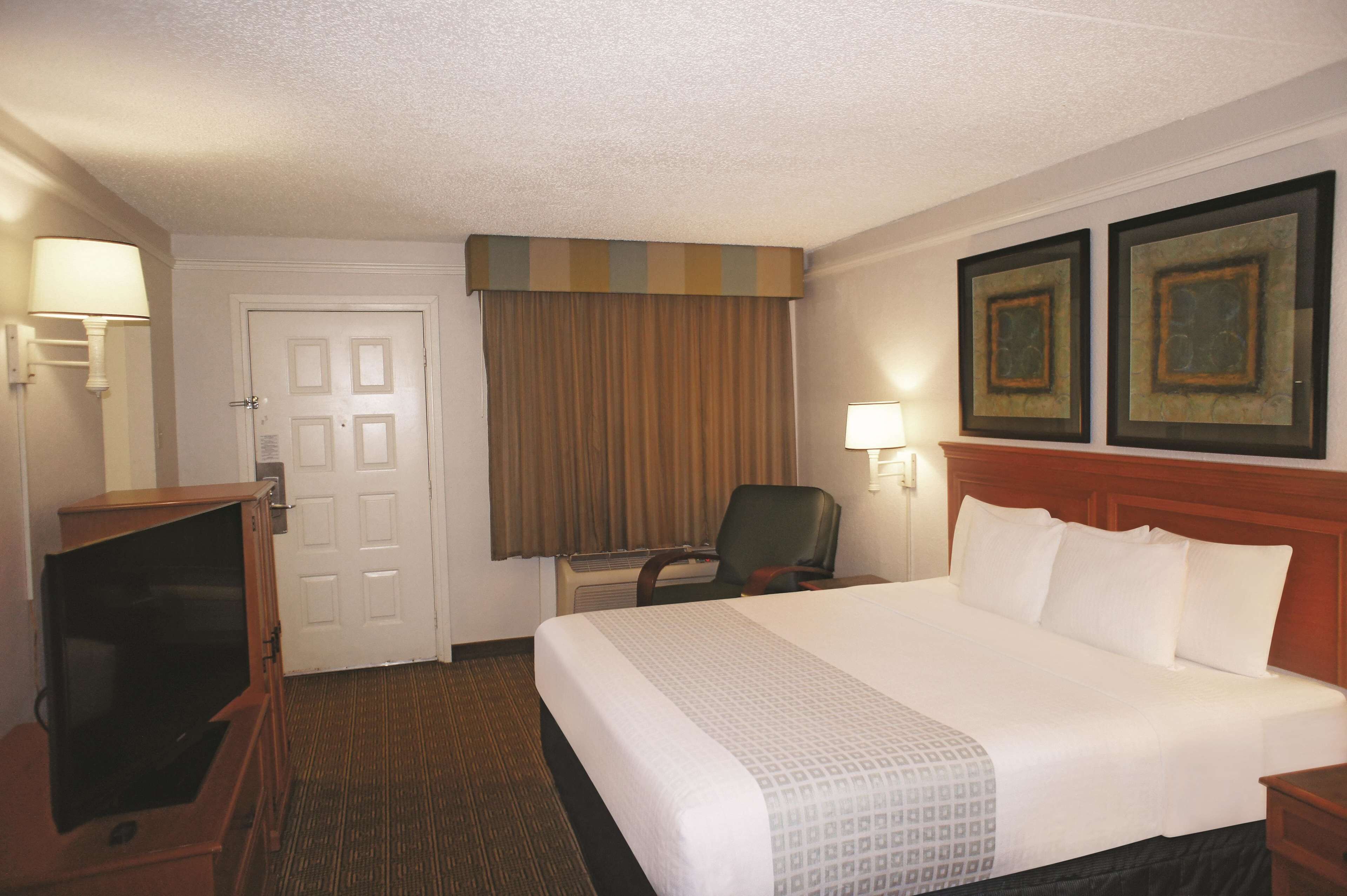 A hotel room with a bed, a desk, a chair, a television, and two framed pictures on the wall.