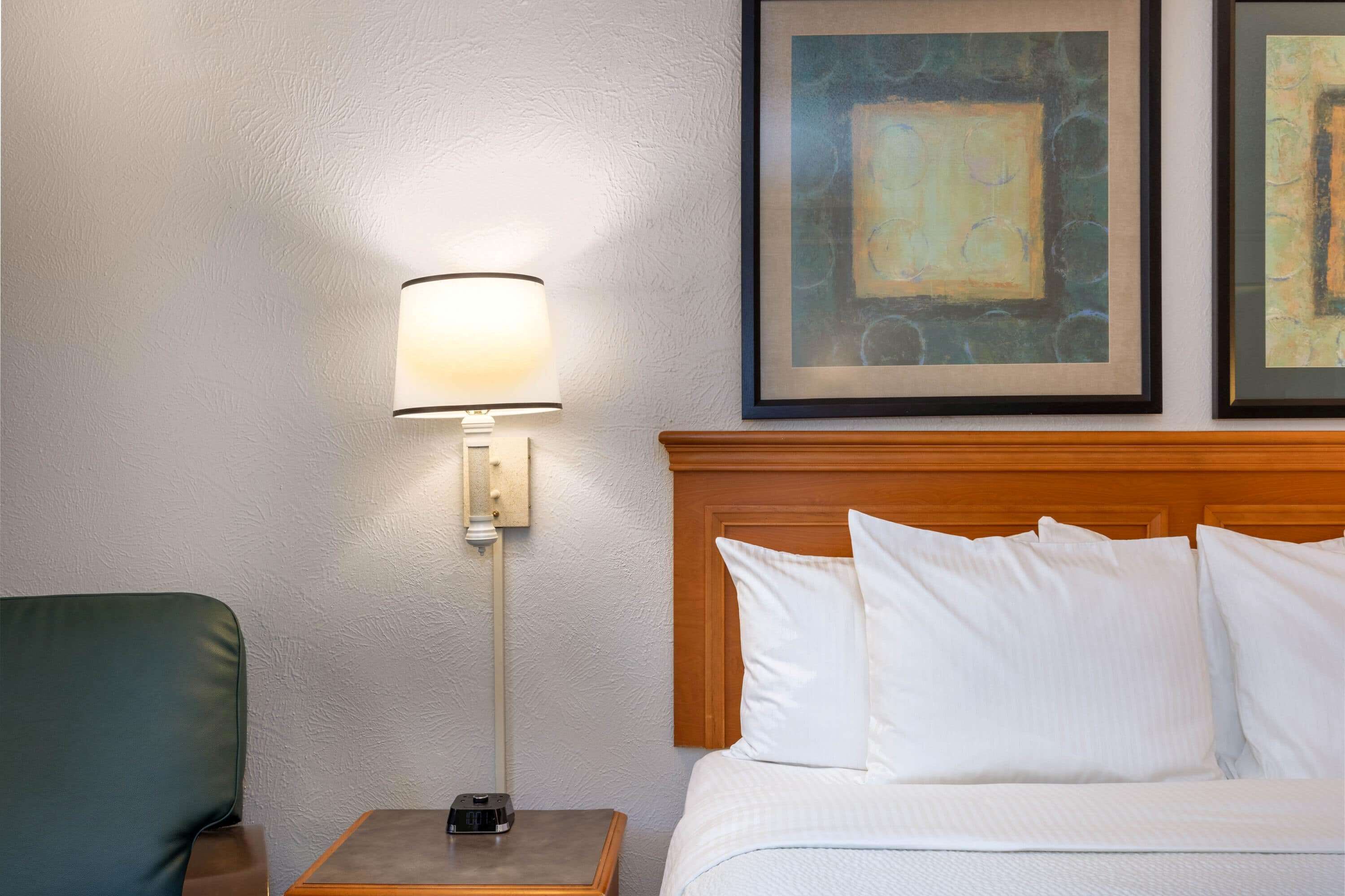 Une chambre d’hôtel avec un lit, une table de chevet avec une lampe et deux œuvres d’art encadrées accrochées au mur.