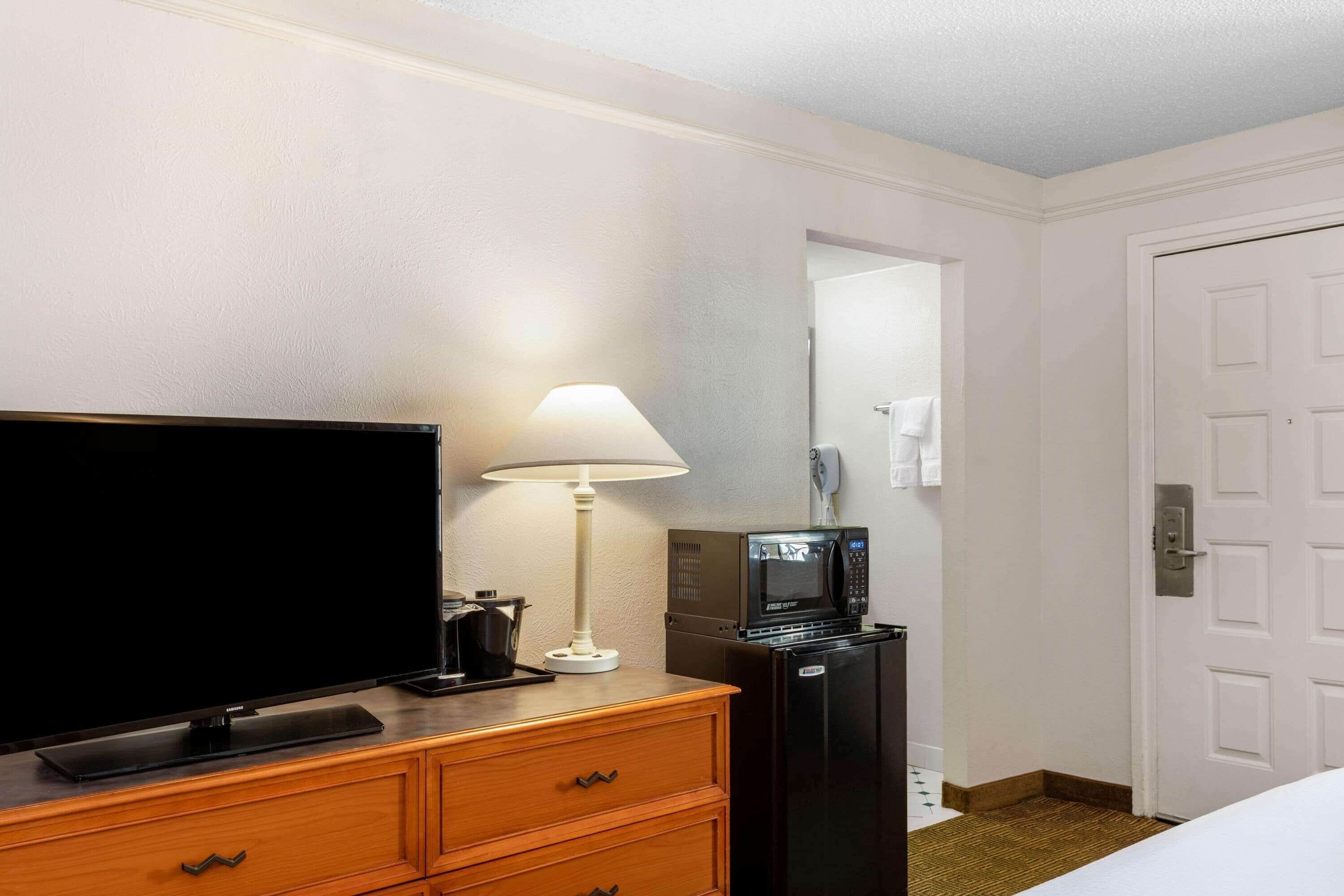 A hotel room with a flat-screen TV, a lamp, a microwave, and a refrigerator.