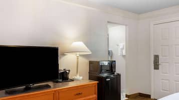 A hotel room with a flat-screen TV, a lamp, a microwave, and a refrigerator.