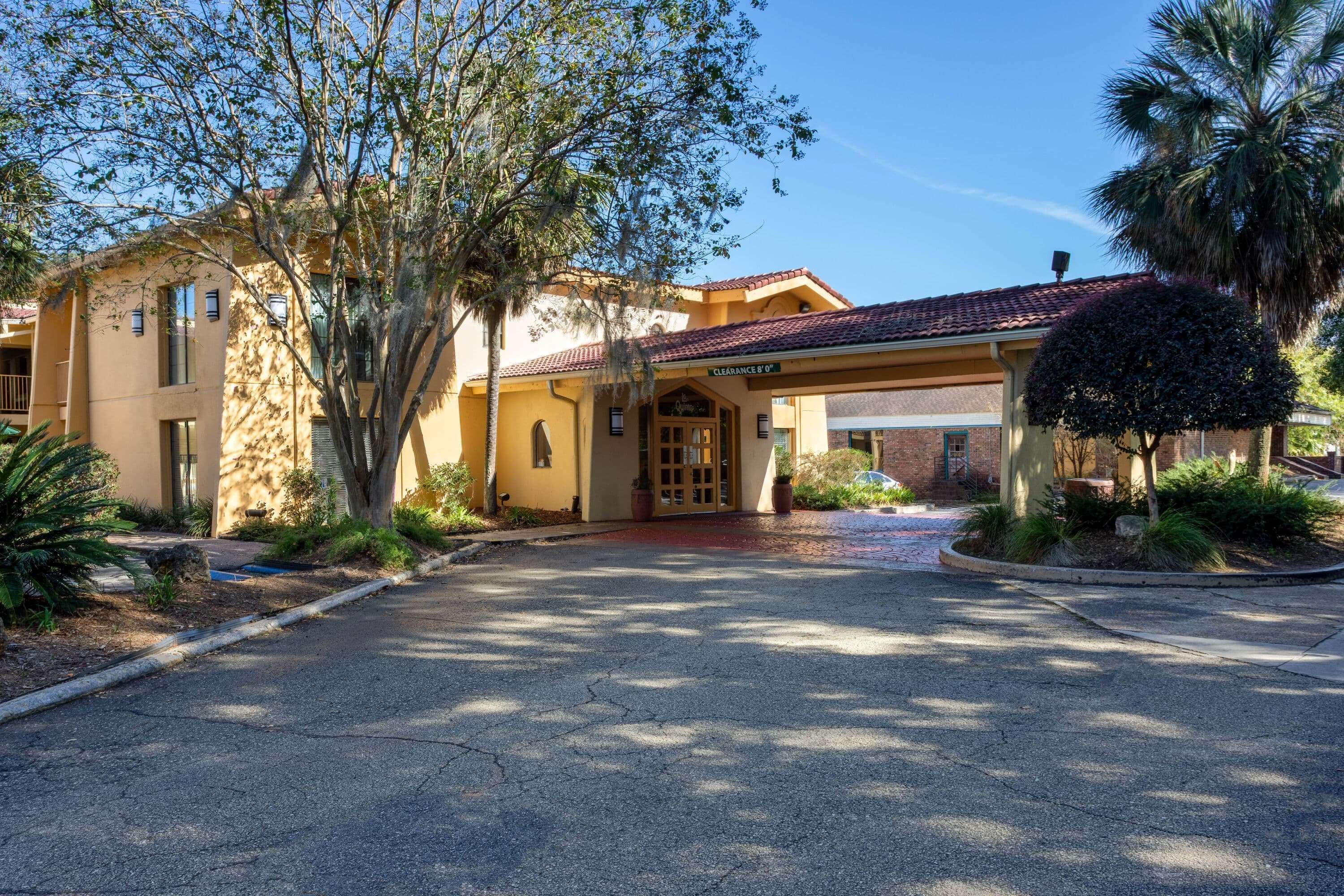 A building with a covered entrance, a clear driveway, and surrounding landscaping.
