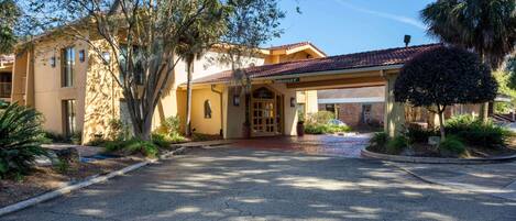 A building with a covered entrance, a clear driveway, and surrounding landscaping.