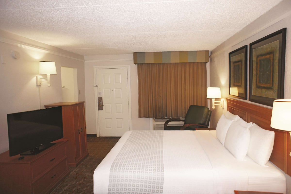 Une chambre d’hôtel avec un lit, un téléviseur posé sur une commode en bois, une chaise et une porte.