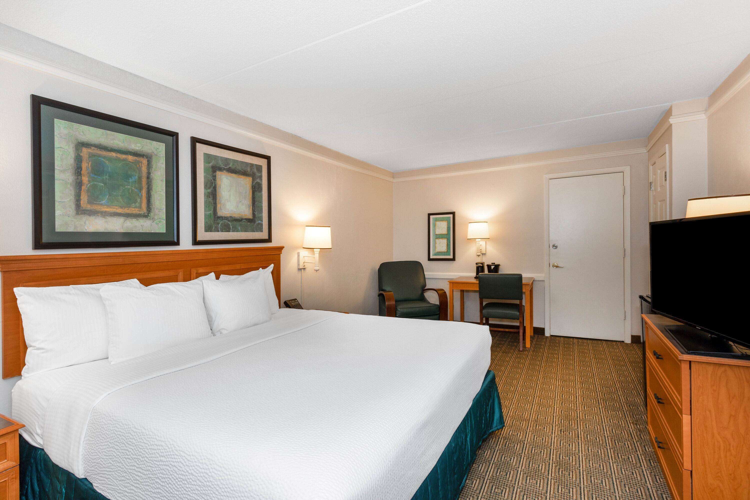 Une chambre d’hôtel avec un grand lit, un bureau avec une chaise, une télévision et deux tableaux encadrés au mur.