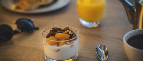 A dessert in a glass, a croissant on a plate, a glass of orange juice, a coffee cup, and a spoon on a wooden table.