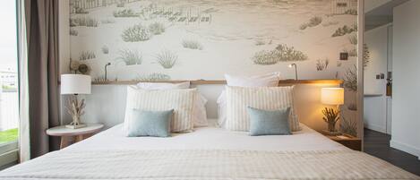 A hotel room with a large bed, two bedside lamps, and a mural of a coastal scene on the wall.