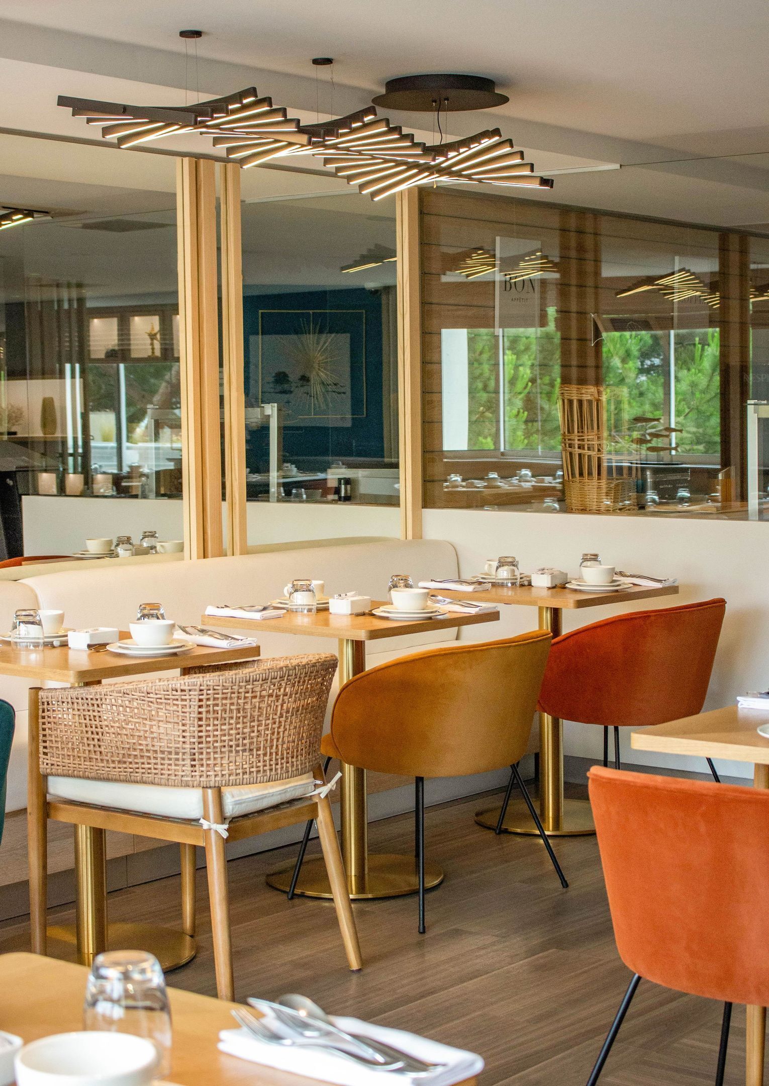 Un espace repas moderne avec des tables en bois, des chaises en osier et une vue sur la verdure environnante.