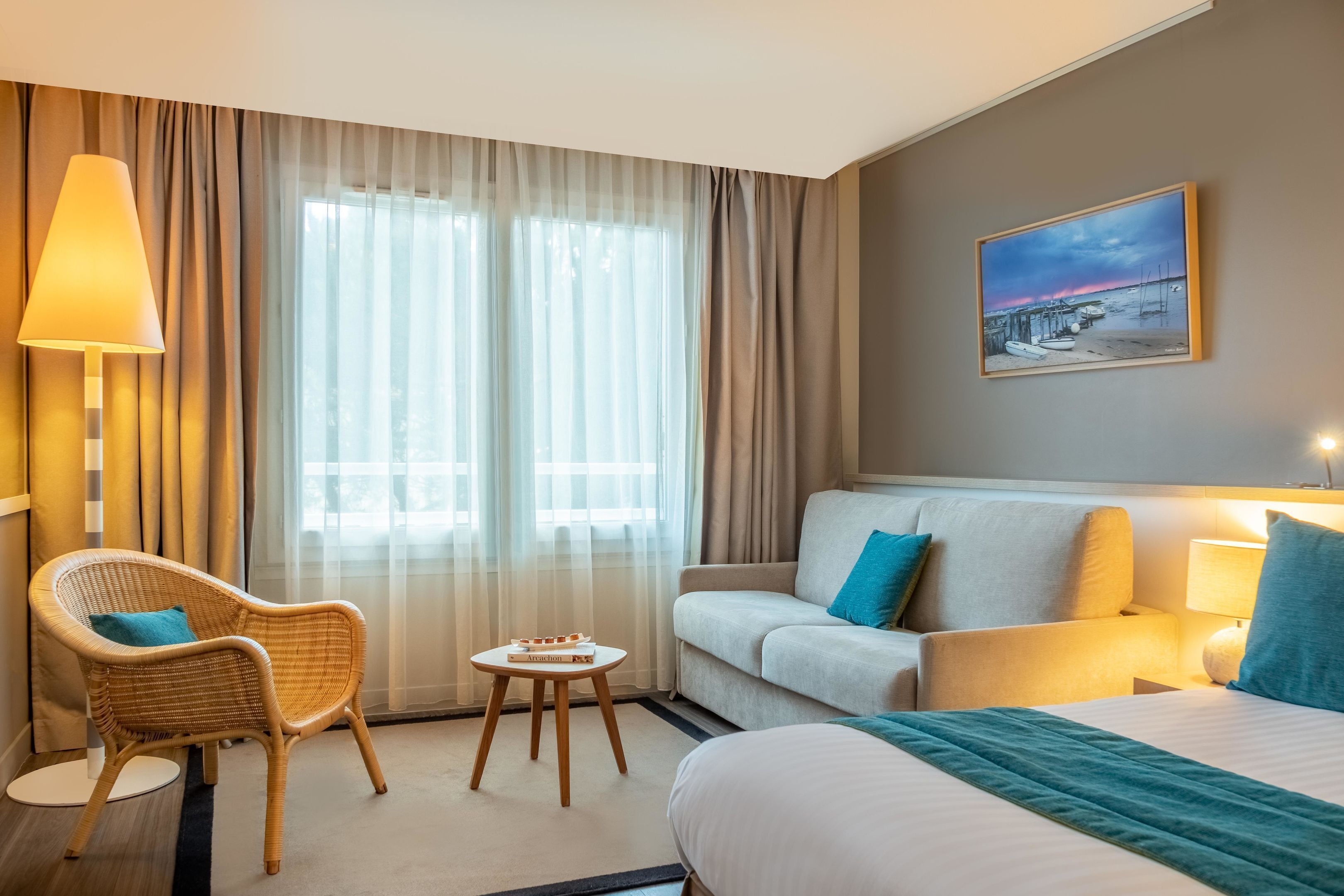 A hotel room with a bed, a sofa, a chair, a small table, and a painting on the wall.