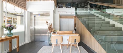A reception area with a reception desk, two chairs, a vase with flowers, and a staircase.