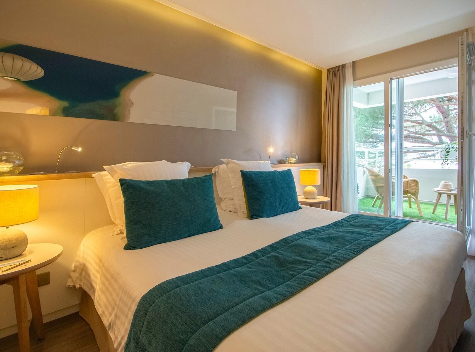 Une chambre d’hôtel avec un grand lit, deux lampes de chevet, une vue sur l’extérieur et un luminaire au plafond.