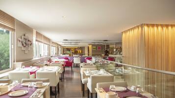 A spacious restaurant with multiple dining tables, chairs, and a glass railing overlooking a scenic view.