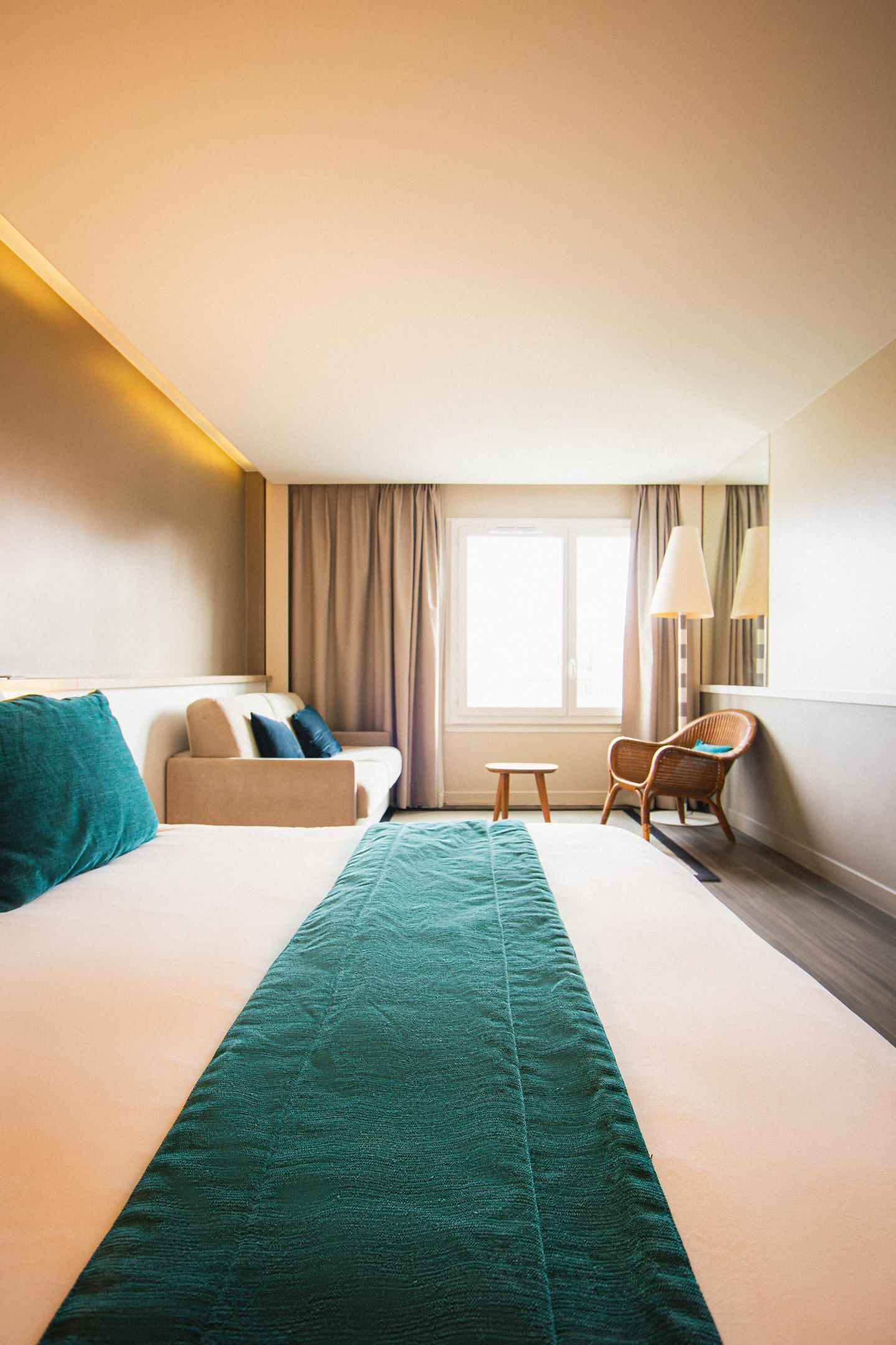 A hotel room with a bed, a sofa, a chair, a small table, and a window with curtains.