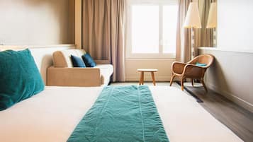 A hotel room with a bed, a sofa, a chair, a small table, and a window with curtains.