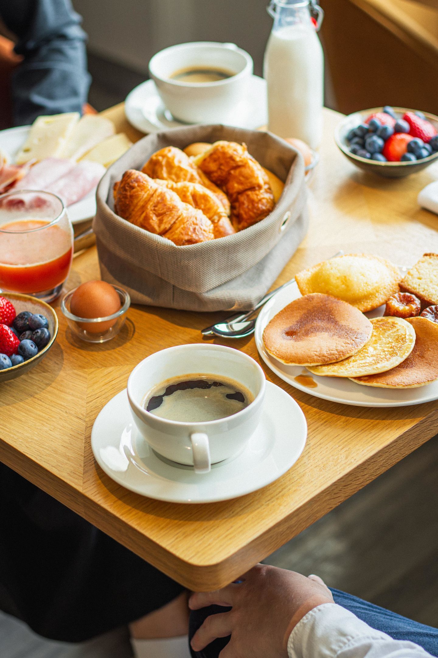 Een ontbijttafel met croissants, pannenkoeken, een koffiekop en een glas sinaasappelsap.