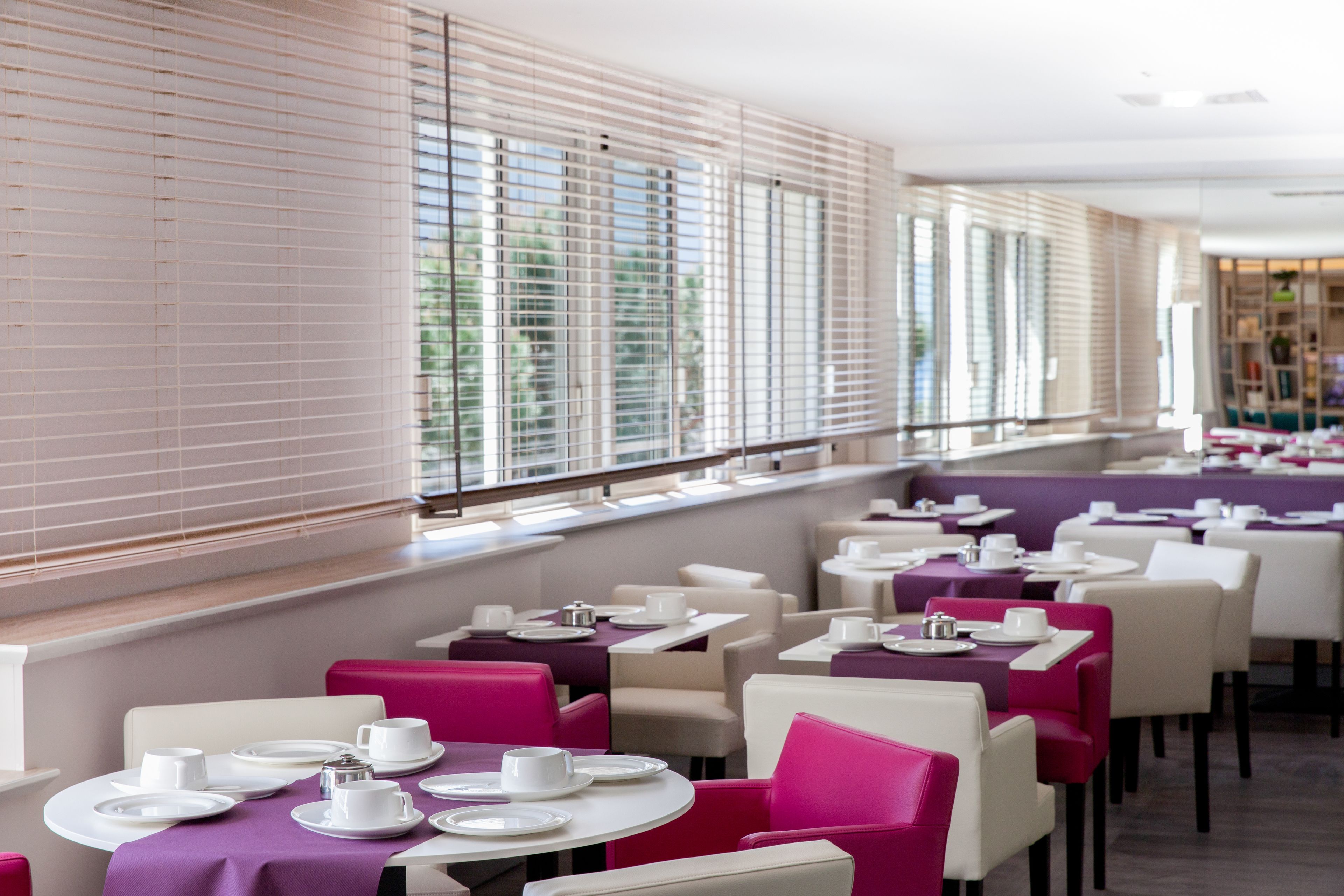 A restaurant with round tables and chairs, some with purple tablecloths.