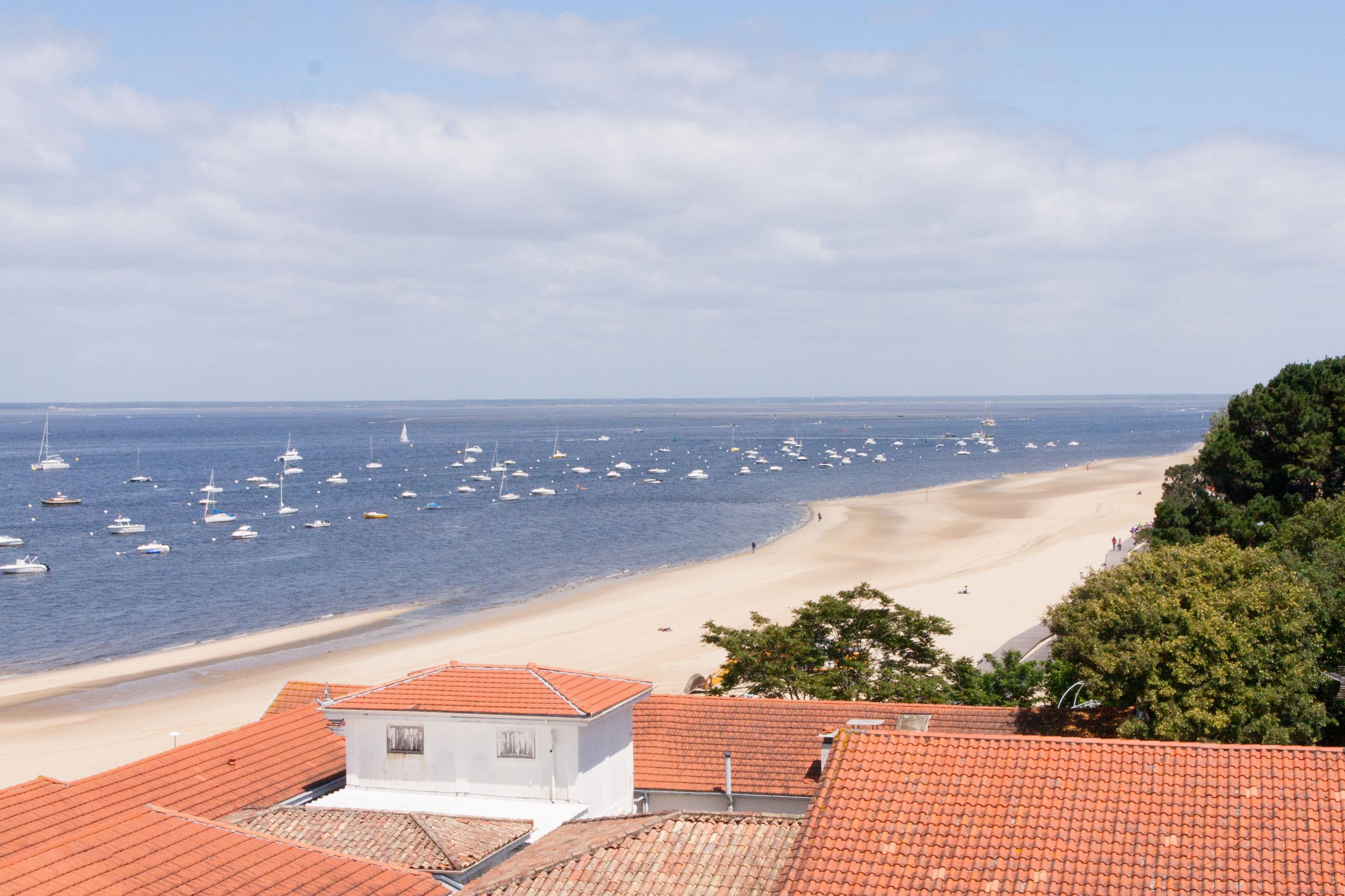 Une vue côtière avec une plage, des bateaux et des bâtiments aux toits recouverts de tuiles rouges.