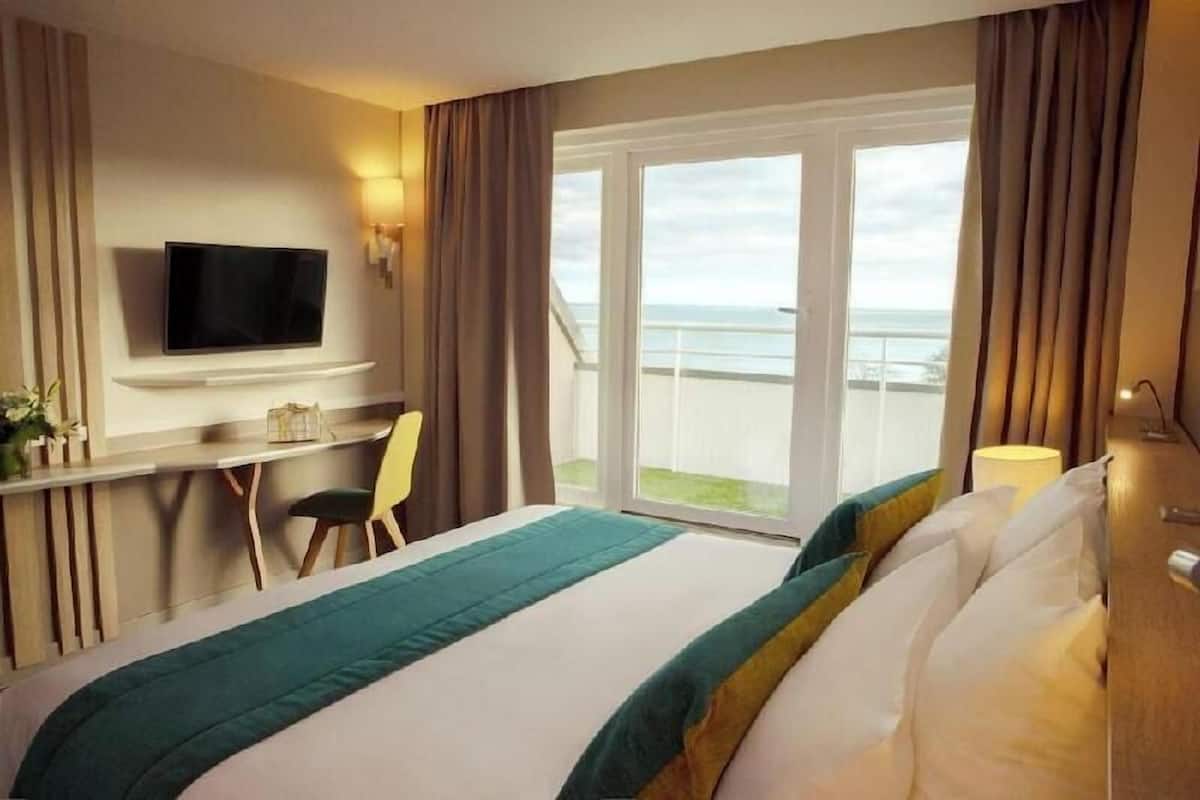 A hotel room with a bed, a desk, a chair, a television, and a balcony with a view.