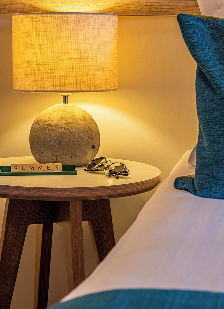 A bed with a blue pillow, a round table with a lamp, and a sign that reads 'SUMMER'.