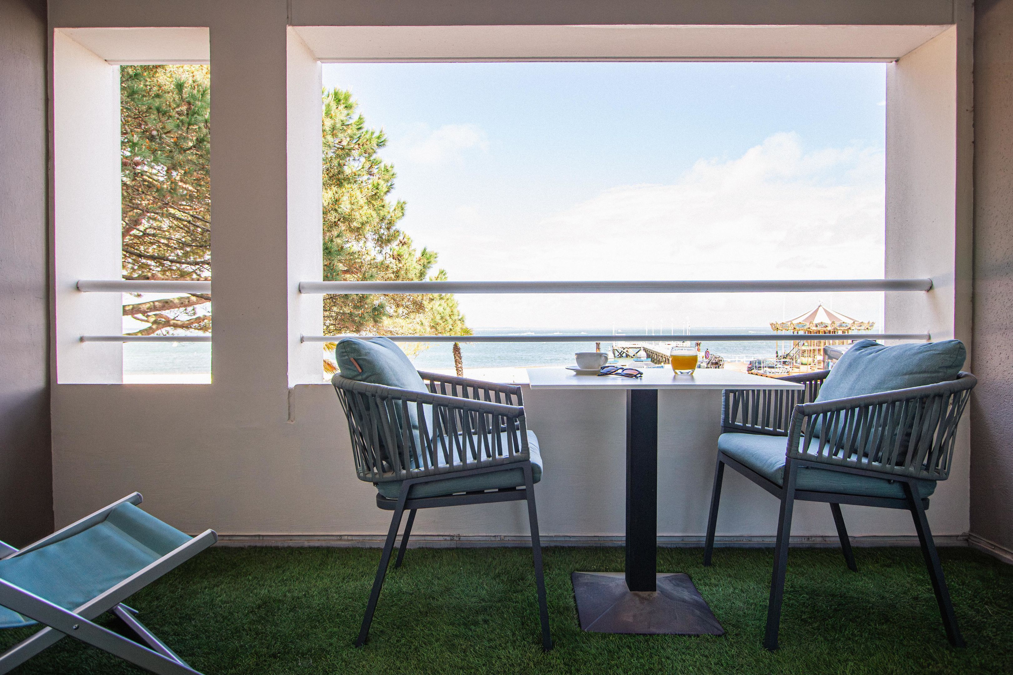 Ein Balkon mit zwei Stühlen, einem Tisch und Blick auf das Meer und einen Steg.