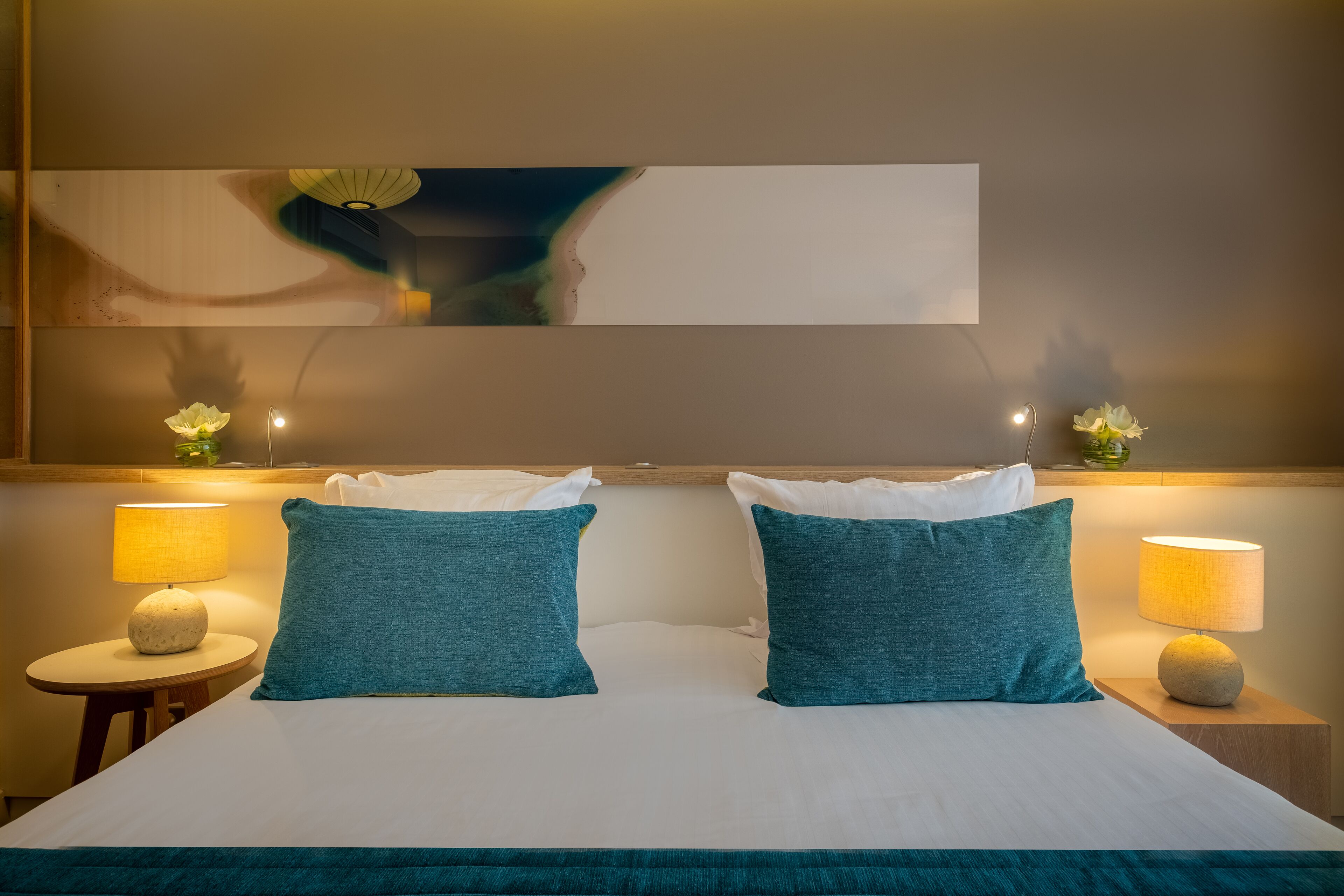 A hotel room with a large bed, two pillows, a nightstand with a lamp, and a wall-mounted mirror.