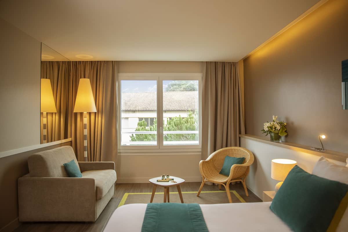 A hotel room with a bed, a sofa, a chair, a small table, and a window with curtains.