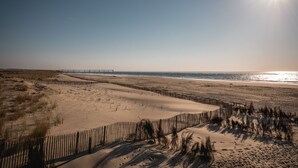 A beach with a wooden fence, sandy dunes, and a bridge in the distance. - Hôtel Le B d’Arcachon by Inwood Hotels (Arcachon)