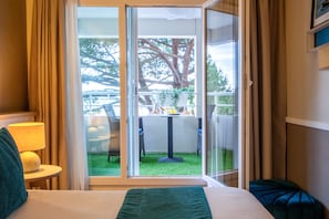 A hotel room with a bed, a nightstand, a lamp, and a view of an outdoor patio with a table and chairs.