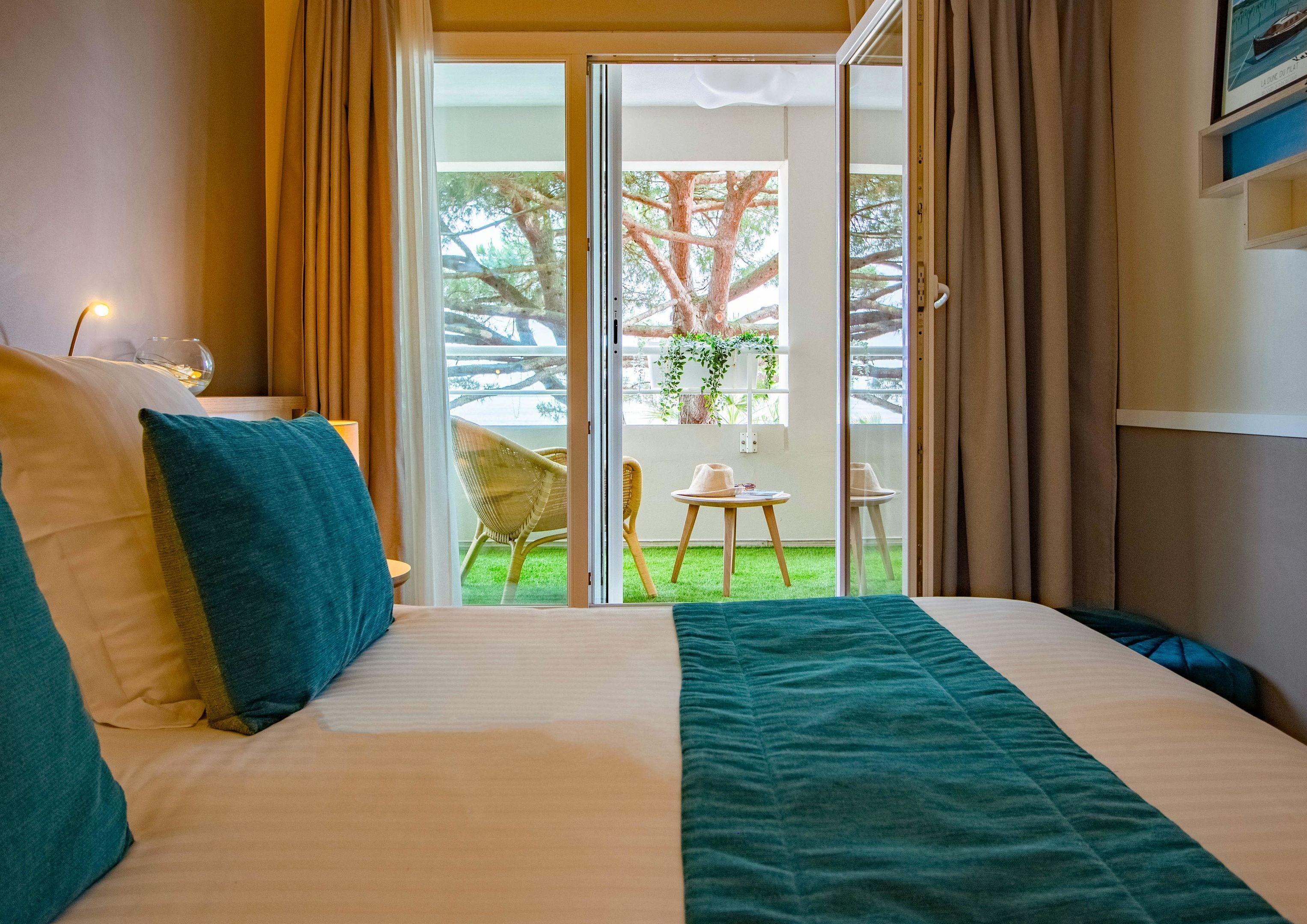 A hotel room with a bed, a view of the outdoors through a sliding door, a chair, and a table.