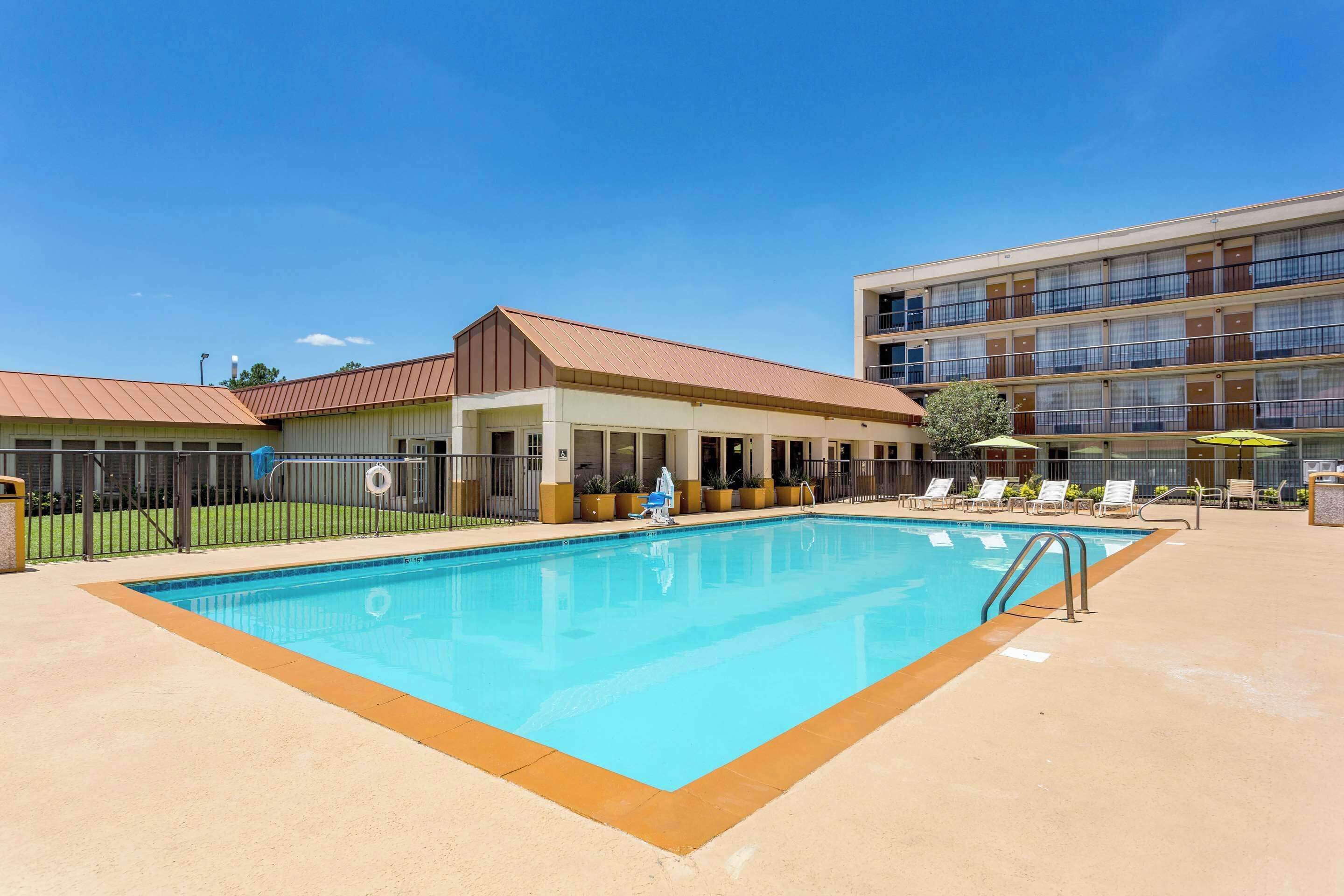 A swimming pool with a fenced area, lounge chairs, and a building with multiple balconies.