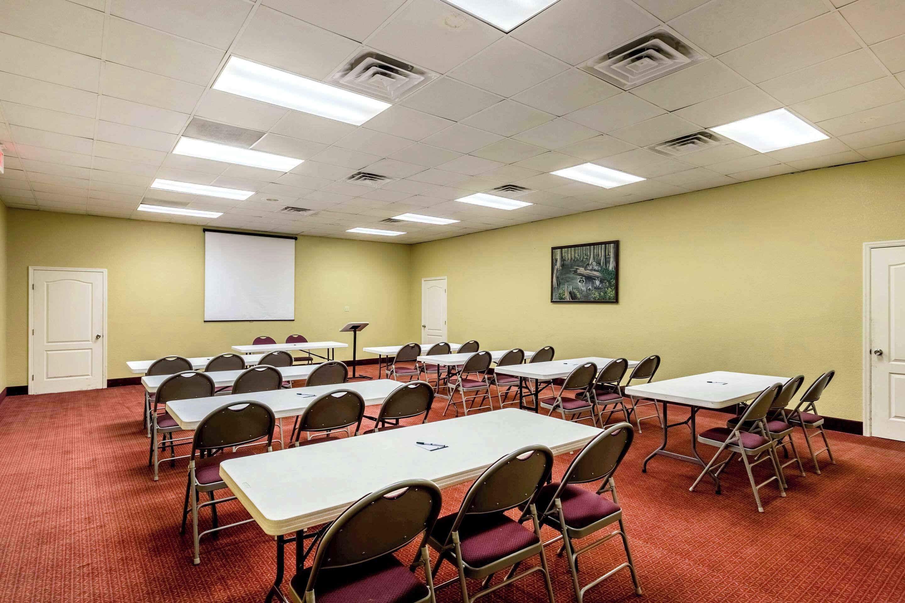 A conference room with multiple tables and chairs, a projector screen, and a whiteboard.