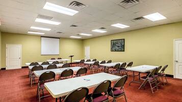 Un salón de conferencias con varias mesas y sillas, una pantalla de proyector y una pizarra.